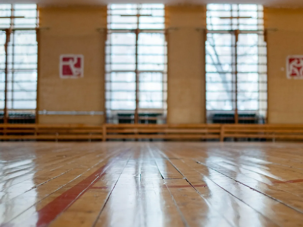 Empty indoor gymnasium with polished wood floor, court markings, and tall windows