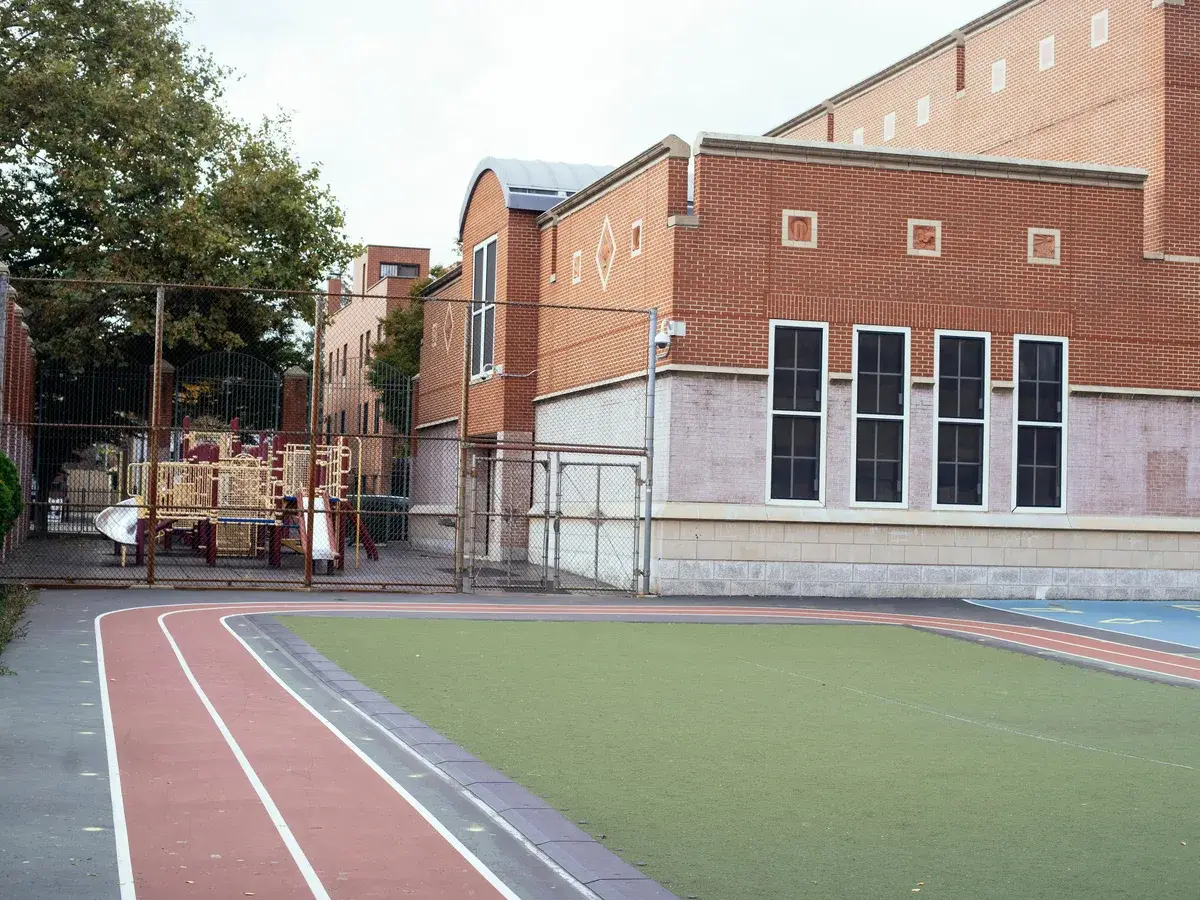 Red brick school building beside an empty schoolyard and playground